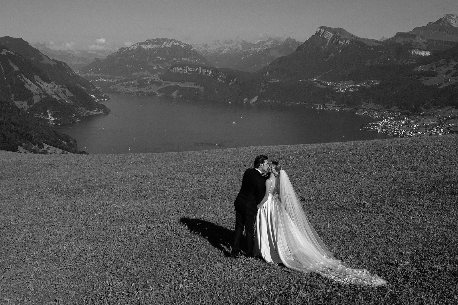 Zwei junge Menschen stehen auf einem Hügel und küssen sich, während sie sich übersehe. Der Mann trägt eine Tuxedo und die Frau eine elegant weiß-blaue Hochzeitsgarderobe.