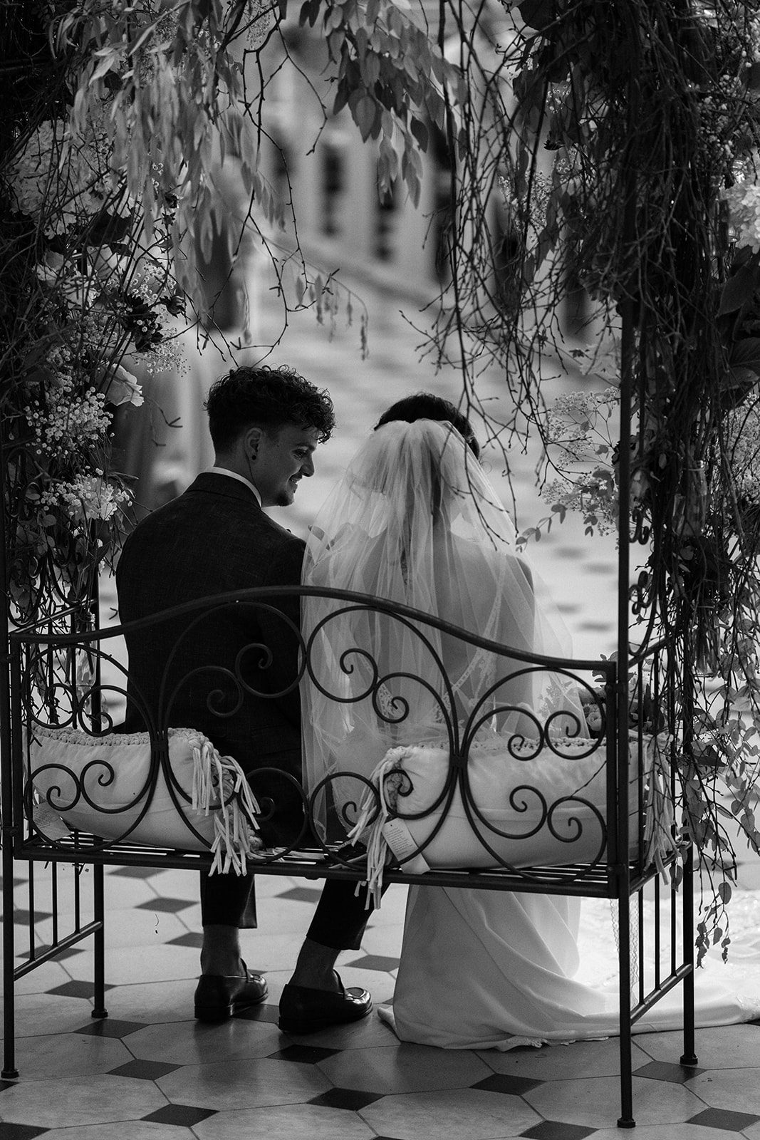 Eine jovielle Ehepaar sitzt in einem Garten-Raum unter einer Pergola und genießt ihre Hochzeitstermine. Der Mann ist im Hut mit der Frau unterhalb des Tisches angesehen, beide sind glücklich und ihr Z